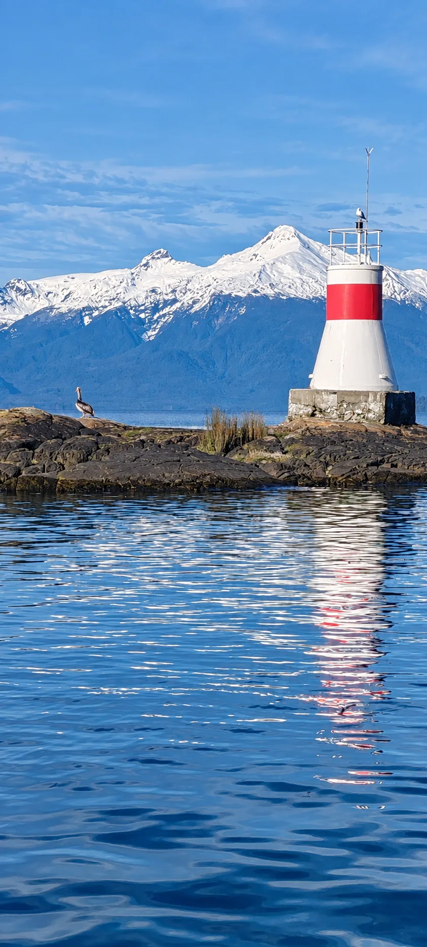 Faro rojo y blanco sobre las rocas, con cerros nevados al fondo
